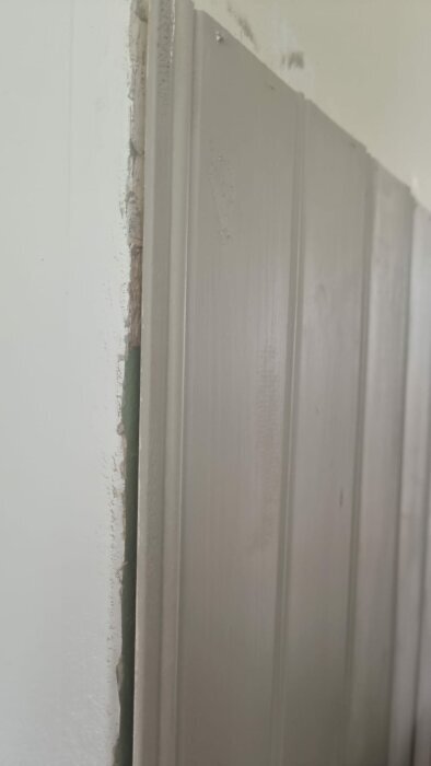 Närbild av en hörna där en vägg med pärlspont möter en obehandlad vägg, med en synlig ofärdig kant mellan materialen.