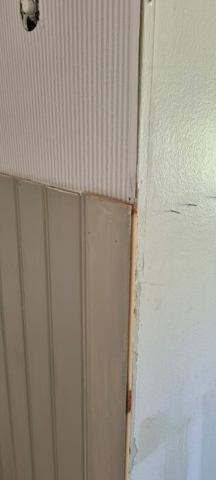 Närbild av ett hörn i en hall där pärlspont möter en slät vägg. Pärlsponten täcker hälften av hörnet och lämnar en synlig rå kant i hörnet.