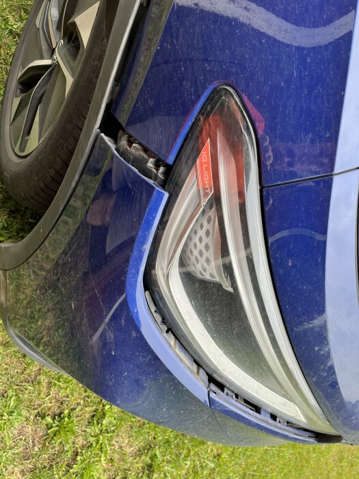 En krockad bakdel av en blå bil som visar skador nära ett bakljus, orsakad av en enstubbe vid backning.