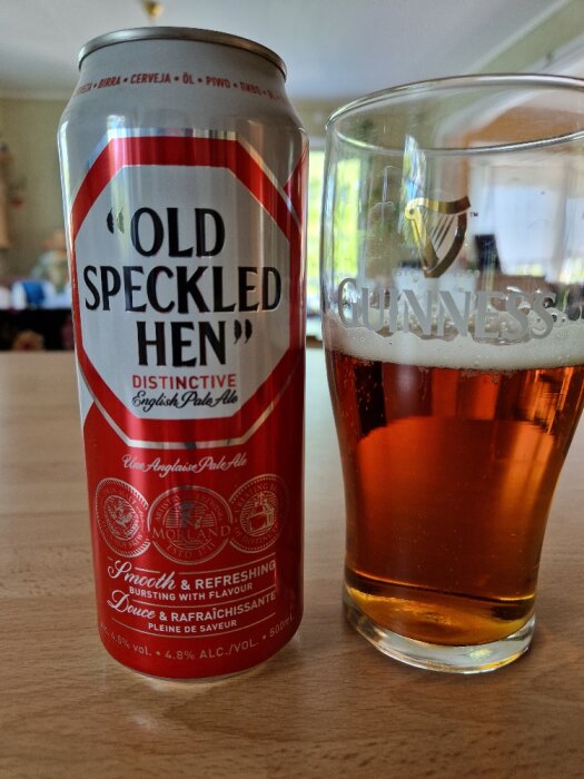 En burk med "Old Speckled Hen" English Pale Ale och ett glas fylld med öl står på ett bord inomhus.