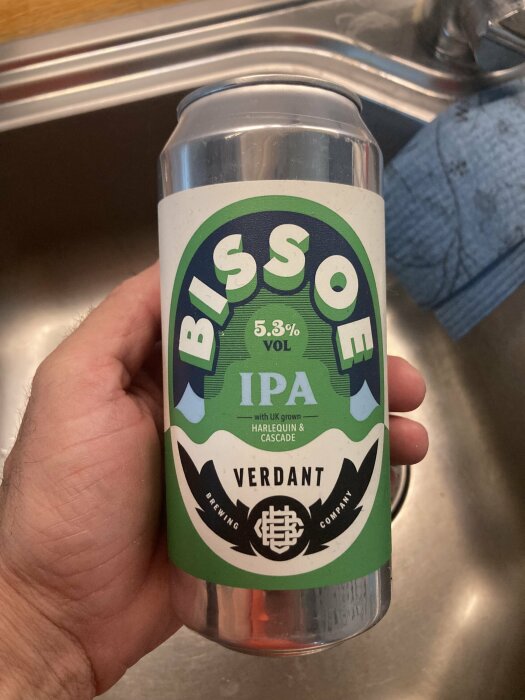 En hand som håller en burk Verdant Bissoe IPA öl med 5,3% alkoholvolym vid en diskbänk.