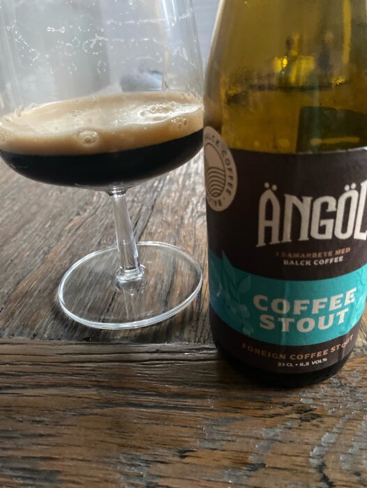 En flaska Ängöl Coffee Stout och ett vinglas med stout på ett trädäcksbord.