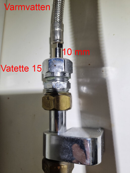 Närbild av en klämringskoppling för varmvatten med texten "Varmvatten", "Vatette 15" och "10 mm" markerad på olika delar av kopplingen.