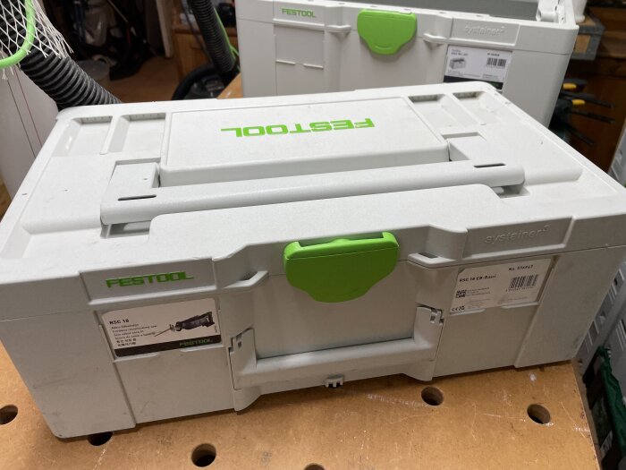 Festool systainer box med grönt handtag på en arbetsbänk i ett verktygsförråd, fler systainer-boxar i bakgrunden.