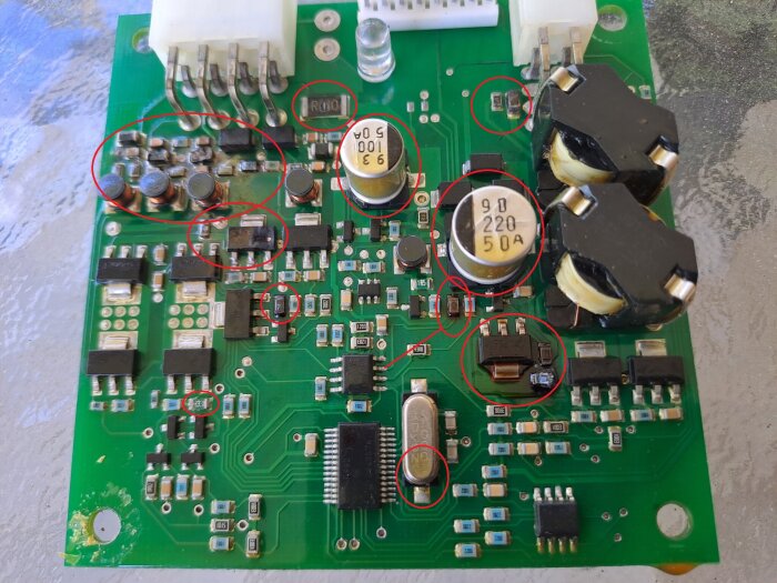 Elektroniskt kretskort med flera komponenter, inklusive kondensatorer, resistorer och anslutningsstift, sittande på ett grönt PCB underlag, med flera markeringar.
