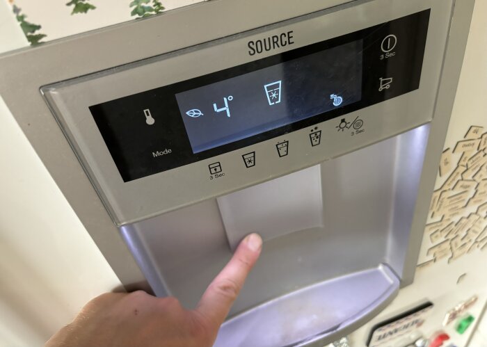 Närbild på en Electrolux kylskåpsdisplay som visar temperatur och ikoner för vatteninställningar, med en hand som pekar på en av knapparna under displayen.