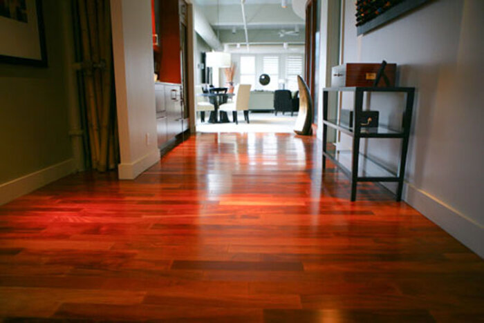 Laminatgolv i körsbärsfärg installerat i en modern korridor som leder till ett ljust möblerat rum i bakgrunden.