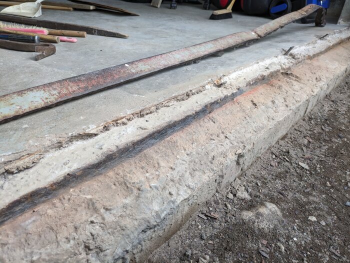 Concrete threshold area with exposed rebar after removal of threshold. Tools lie nearby on the ground.