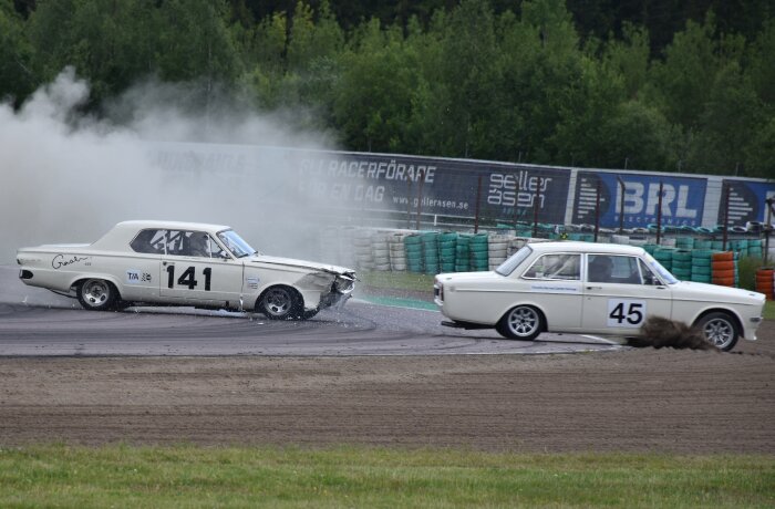 En vit bil med nummer 141 krockar med en annan vit bil med nummer 45 under Velodromloppet i Karlskoga, med rök och damm bakom dem.