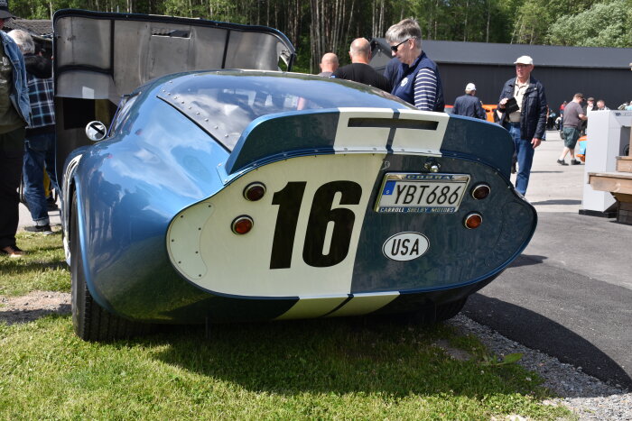 Blå Shelby Cobra med nummer 16 och registreringsplåt "YBT 686" USA, parkeras på gräs med människor i bakgrunden på Velodromloppet i Karlskoga.