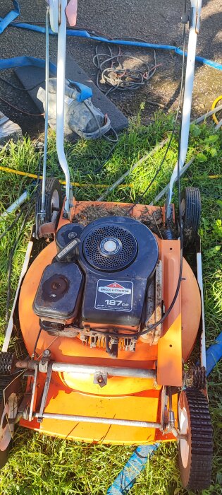 Gammal orange Husqvarna gräsklippare med en Briggs & Stratton 187cc motor på 4 hästkrafter. Gräsklipparen är placerad på en gräsmatta med verktyg runtom.