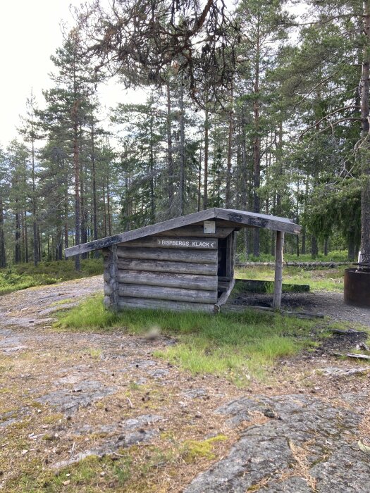 Liten trähytt markerad med en skylt som säger "Bispbergs Klack" omgiven av tallskog.