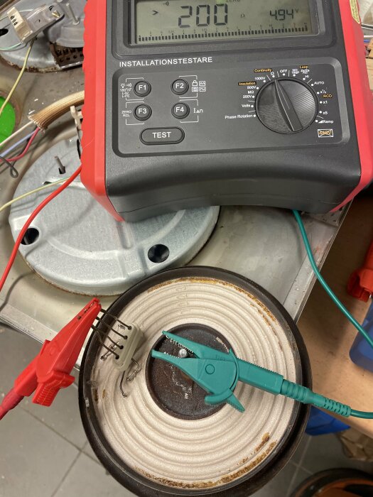 Multimeter mäter resistansen i en av plattorna från en gjutjärnsspis utrustad med två testprober. Multimetern visar ett mätvärde på 200 ohm.