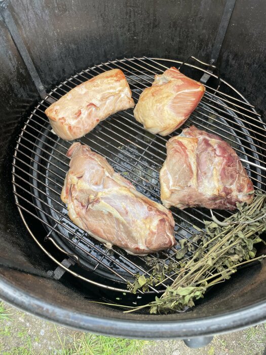 Köttbitar av vildsvin och annat kött ligger på en gallergrill inne i en rök, med en bunt örter bredvid köttet.