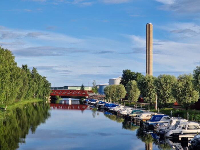 Nya Engholmsbron i Karlstad över en spegelblank kanal, träd längs kanalen och sommarhimmel i bakgrunden.