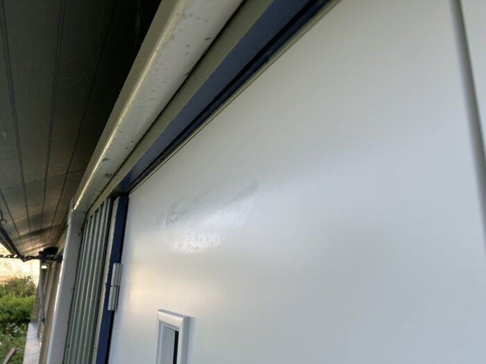 Närbild på vit ytterdörr från Safco, där en lackdefekt syns tydligt på ytan, installerad i dörrkarmen under ett grått tak.