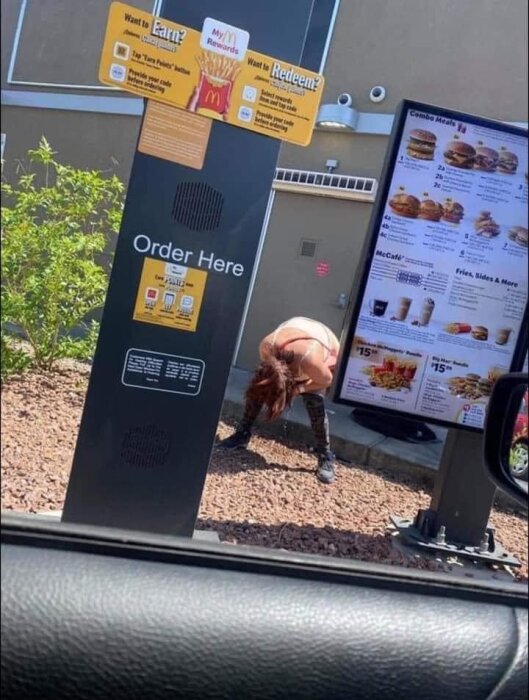 En kvinna böjer sig ner bredvid en drive-through meny och beställningsskärm på McDonald's.