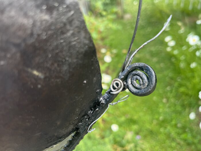 Närbild på en skulptur av en fjäril i metall, med detaljerade, spiralformade antenner och en suddig grön bakgrund.