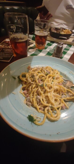 Tallrik med spaghetti carbonara och ett glas öl på en restaurang.