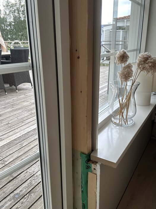 Närbild på två dörrar bredvid varandra mellan vardagsrum och altan med en träram i mitten. Dekorativa torkade växter i glasvas på fönsterbrädan till höger.