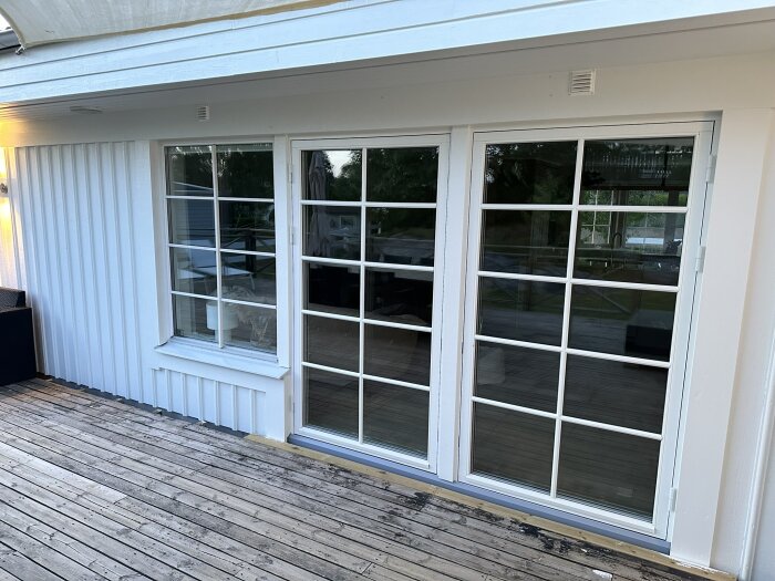 Två 120 cm breda vita dörrar med spröjsade fönsterrutor installerade på en vit fasad, med en träaltan framför.