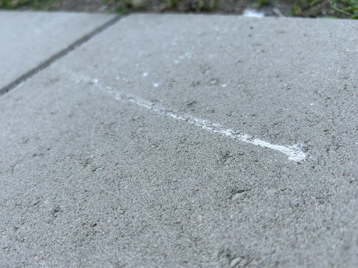 Närbild på ljusgrå betongplattor med en lång, vit skrapmärke på ytan. Plattorna har mindre fläckar och ojämnheter.