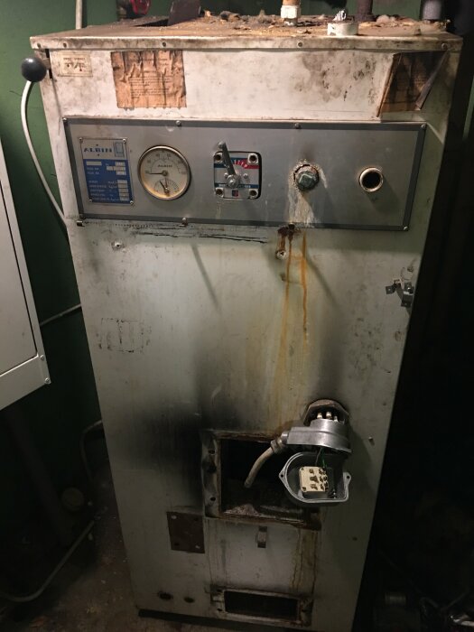 En oljebrännare av märket Albin från 1973, placerad vid en källartrappa, med demonterade delar och tydliga rostfläckar.