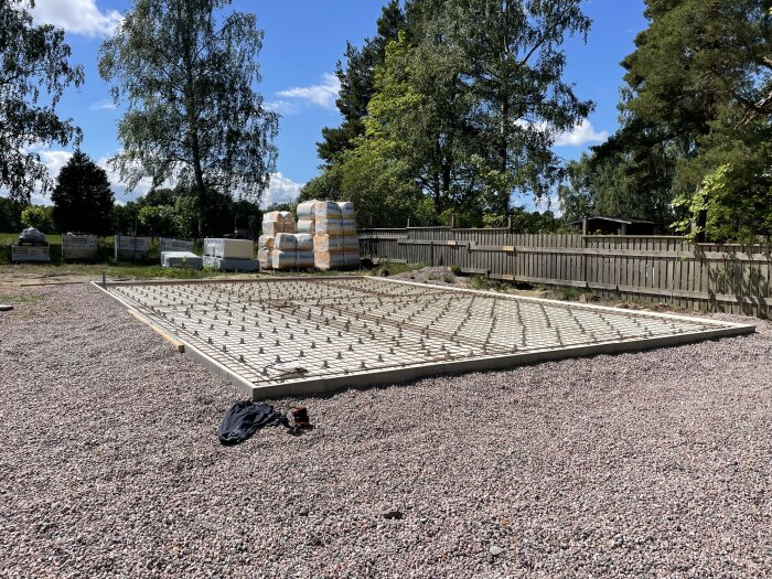 Betonggrund med kantelement för ett garage/verkstad på 80m2, omgiven av träd och byggmaterial, redo för gjutning.