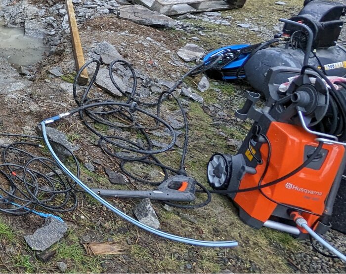 En tryckluftskompressor, slangar och verktyg på marken vid ett spräckt berg. Vattenfyllda hål och grus runt omkring avslöjar arbete med snigeldynamit.