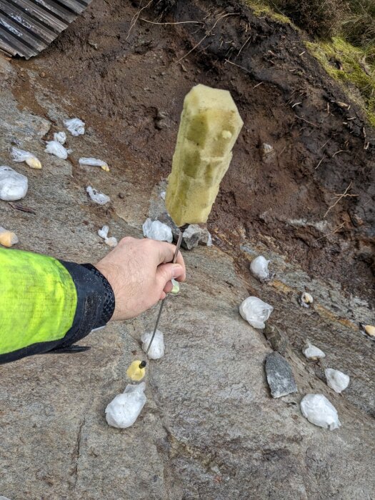 Hand som håller en "ikeapinne" med svamp i ändan för att torka hål borrade i berg, omgivna av plastpåsar fyllda med isolering.