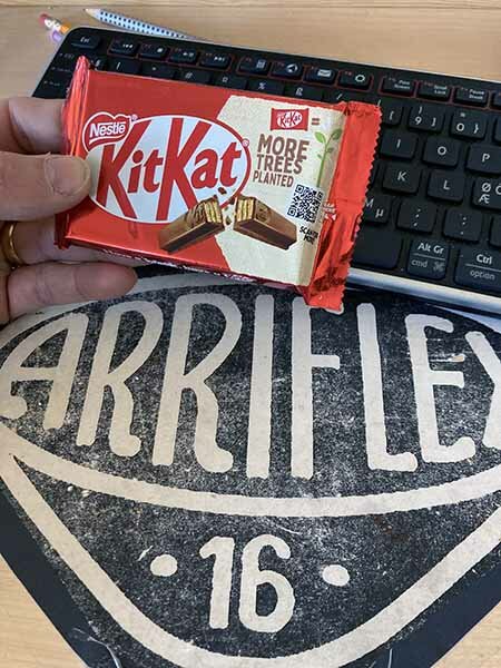 En hand håller en Kit Kat-chokladkaka framför ett bord med ett Arriflex 16-underlägg och en tangentbord i bakgrunden.