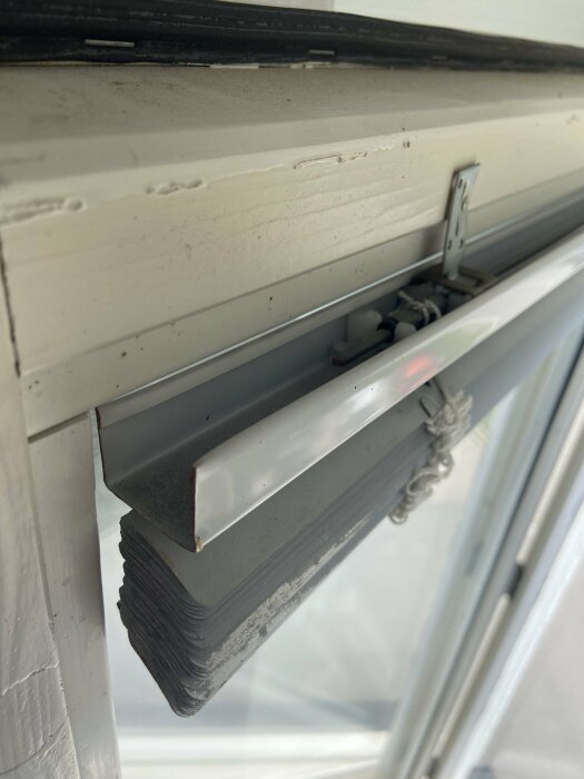 Närbild av fastspikad persiennhållare i en fönsterkarm med en persienn hängande nedanför.