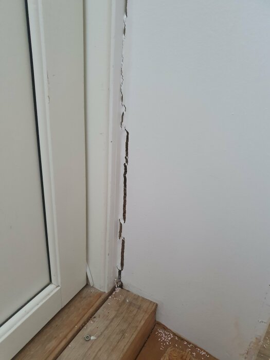 Spricka mellan yttervägg och sidokanten på en köksbänk bredvid en vit dörrkarm, med trätröskel och lite sågspån på golvet.