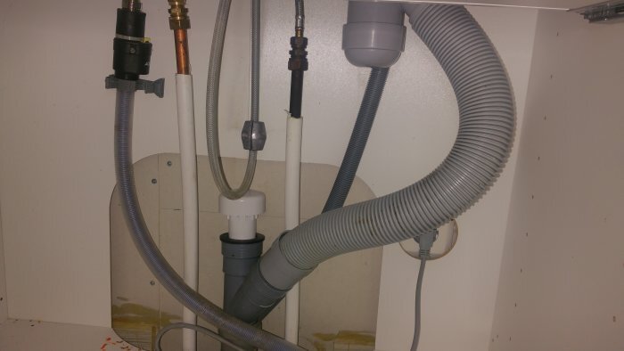 Avloppssystem under köksbänk med flera rör och en vakuumventil synlig installerad.