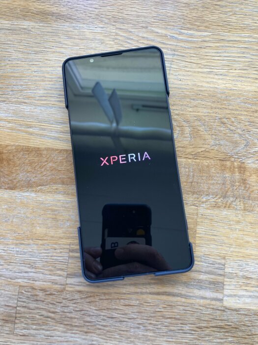 En Xperia 1 VI mobiltelefon i svart färg placerad på ett träbord. Skärmen är avstängd och reflekterar omgivningen.