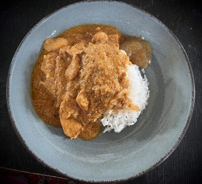 En tallrik med butter chicken och ris, serverad med mango chutney på sidan.