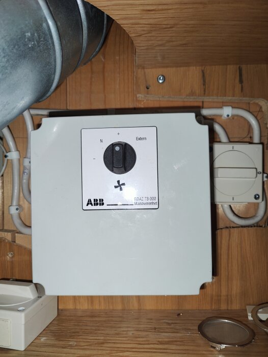 Manöverpanel för ventilation med inställningsknapp och kablar, monterad på vägg.