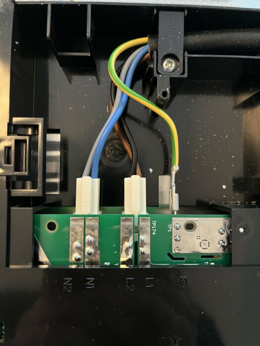 Elektrisk anslutningsbox med kablar anslutna till terminaler märkta N, L, och jord. En brun, blå och grön/gul kabel syns.