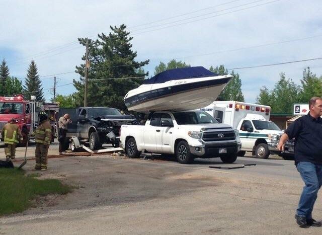 En vit pick-up med en båt på sitt flak har krockat med en svart pick-up. Räddningspersonal och utryckningsfordon finns på plats.