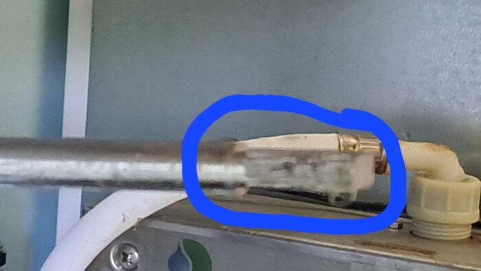 Närbild av en metallaxel från ett tvätthoavlopp, inringad med en blå cirkel. Avfasning på axeln är synlig men suddig.