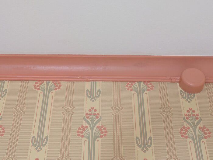 Målade kablar längs en vägg med blommig tapet och en orange målning längs golvlisten. En rund kopplingsdosa syns i högra hörnet.