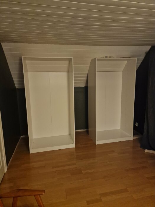 Två ofullständigt monterade IKEA-garderober placerade i ett rum med snedtak och träfärgat golv.