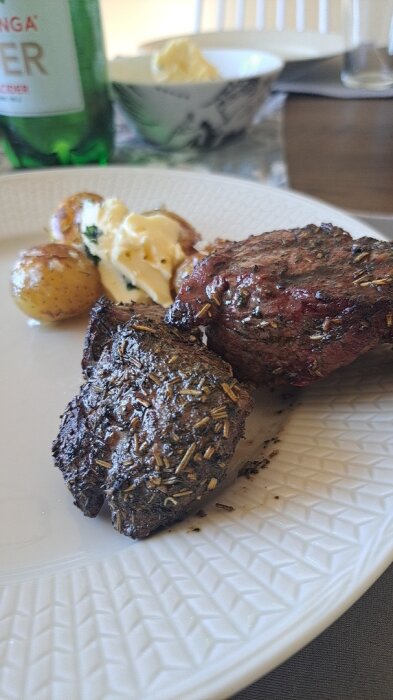 Grillat lamm serverat med ugnsrostad potatis och en klick bearnaisesås på en vit tallrik; flaska mineralvatten i bakgrunden.