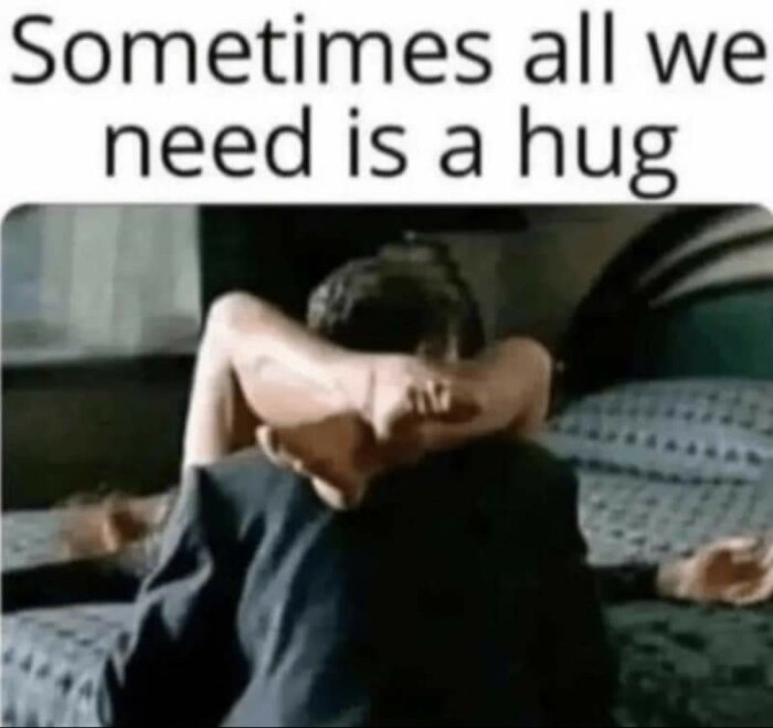 En person sitter på en säng medan en annan person ger en kram bakifrån. Texten "Sometimes all we need is a hug" är ovanför bilden.