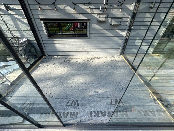 Vindpapp av märket Mataki W7 installerad på golv på en insynad veranda, med glasväggar och sikt mot trädgården.