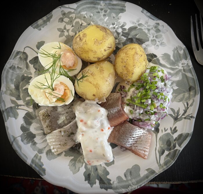 En tallrik med tre sorters sill, färskpotatis, ägghalvor med räkor och dill samt rödlök och gräslök på crème fraiche.