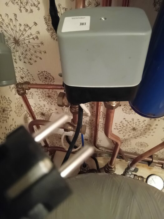 En kopplingsdosa och en kontakt i ett badrum med synliga rör och ledningar, potentiellt kopplad till en hydrofor.