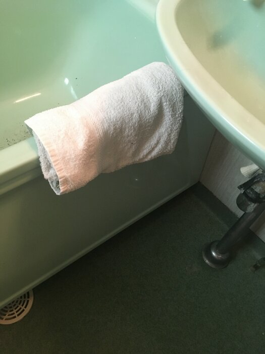 Grönt badkar med vit handduk, grönt handfat och grönt golv i ett äldre badrum.
