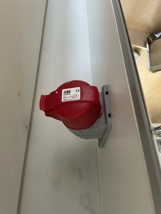 Röd byggcentral kontakt med märkningen ABB 416RS6 monterad på en vägg i ett elskåp.