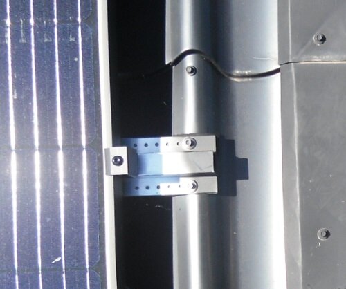 Närbild på metallfäste skruvat i en takplåt, med en solpanel monterad till vänster.